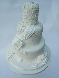 a three tiered wedding cake with white flowers and pearls on the top, sitting on a plate