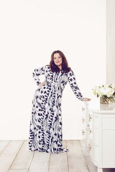 a woman in a long dress standing on a wooden floor next to a white dresser