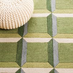 a green and white rug on the floor next to a round ottoman with a knitted cushion