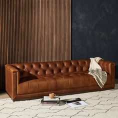 a brown leather couch sitting on top of a white rug next to a wooden wall