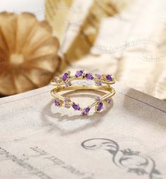 a gold ring with amethyst purple stones on top of an open book next to a golden vase