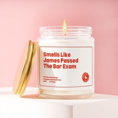 a candle that is sitting on top of a table next to a jar with the label smells like james passed the bar exam