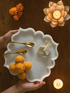 a person holding a white plate with some food on it and candles in the background