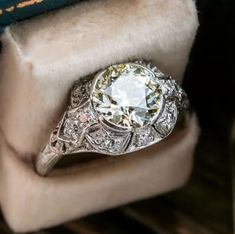 an old - fashioned diamond ring sits on top of a velvet covered box with a book in the background