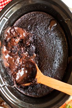 a wooden spoon stirring chocolate cake batter in a crock pot with red and white checkered table cloth