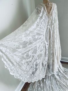 a white dress with sheer lace on the bottom, and an open cape over it