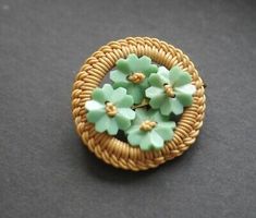 a green flower brooch sitting on top of a black table next to a basket