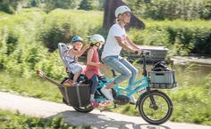 two children riding on the back of a bike with their mom and dad behind them