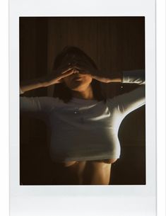 a woman in white shirt holding her hands up to her face while standing next to a wooden wall