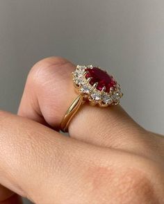 a woman's hand holding a ring with a red and white stone in it