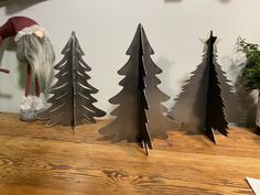 three metal christmas trees on a table next to a santa claus hat and other decorations