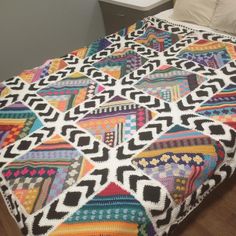 a multicolored quilt on a bed in a room with white walls and wood flooring