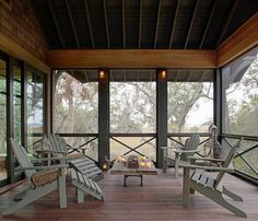 two chairs and a table on a porch with wood flooring, overlooking the trees