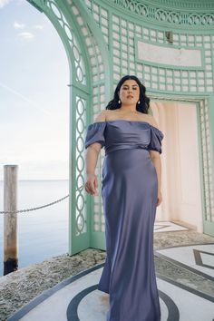 a woman in a blue dress posing for a photo by the water with her hands on her hips