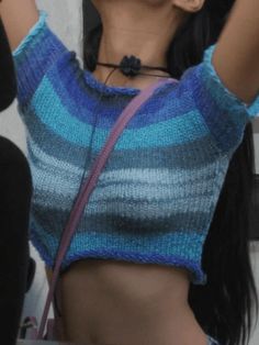 a woman with long black hair wearing a blue and grey striped sweater holding her hand up in the air