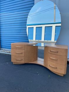 a mirror sitting on top of a wooden dresser next to a blue building with shutters