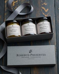 three jars of preserves in a gift box on a wooden table next to a ribbon