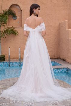 a woman standing in front of a pool wearing a wedding dress with an open back