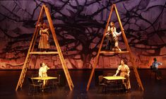 three people sitting on top of wooden ladders in front of a stage with purple walls