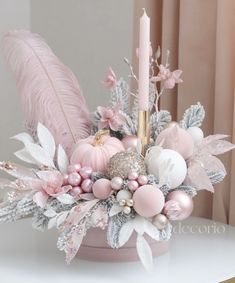 a candle is sitting on top of a table with pink flowers and feathers in it