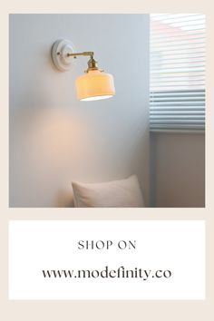 a white lamp on the wall next to a pillow and window with blinds in it