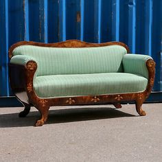 an old wooden couch sitting in front of a blue metal wall with peeling paint on it