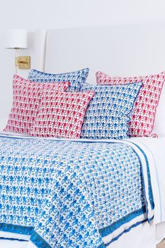 a bed with red, white and blue pillows on top of it next to a night stand