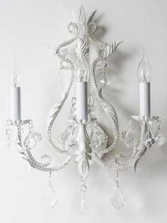 a white chandelier hanging from the side of a wall with two candles on it