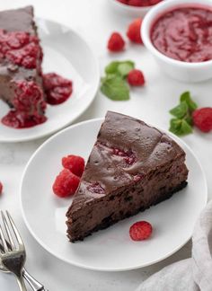 a slice of chocolate cake with raspberries on the side and another piece missing