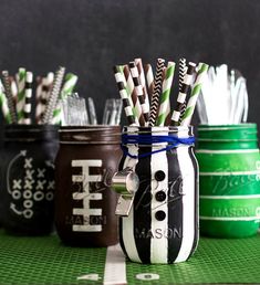 four mason jars filled with striped straws on top of a green tableclothed surface