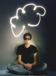 a man sitting on the floor in front of a black background with glowing clouds above him