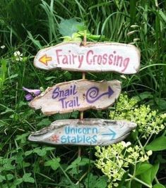 three wooden signs pointing in different directions on the grass and flowers behind them are plants