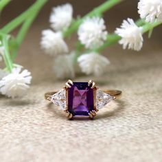 an amethorate and diamond ring sitting on top of a table next to flowers