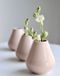 three pink vases with flowers in them on a white countertop, one is empty