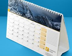 a desk calendar on a blue background with the image of mountains and clouds in it