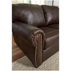 a brown leather couch sitting on top of a carpeted floor next to a window