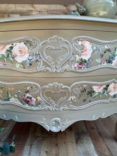 an old dresser with flowers painted on the top and bottom, sitting on a wooden floor