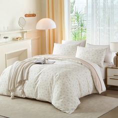 a bed with white comforter and pillows in a room next to a window,