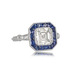 This geoemtrically designed engagement ring features a 2.01 carat asscher cut diamond with J color and VS2 clarity. Surrounding the center diamond is a halo of natural calibre French-cut sapphires with a vibrant blue saturation. The triple wire shank leads to accenting stones on either shoulder, with beautiful a openwork filigree under-gallery. ✦ DIAMOND SPECIFICATIONS: Diamond Cut: Asscher Cut Diamond Clarity: VS2 Diamond Color: J Color Diamond Weight 2.01 Carats ✦ ENGAGEMENT RING SPECIFICATION Gia Certified Cushion Cut Sapphire Ring In Platinum, Luxury Octagon Brilliant Cut Sapphire Ring, Luxury Octagon Sapphire Ring With Brilliant Cut, Luxury Gia Certified Octagon Sapphire Ring, Gia Certified Octagon Sapphire Luxury Ring, Gia Certified Octagon Sapphire Ring, Luxury Style, Luxury Octagon Sapphire Platinum Ring, Luxury Gia Certified White Sapphire Ring, Luxury Octagon Sapphire Ring In Platinum