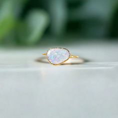 a white opal ring sitting on top of a marble table next to a green plant