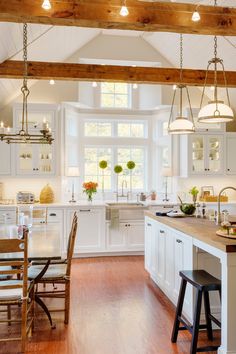 a large kitchen with white cabinets and wood flooring is pictured in this image, there are two stools at the center of the island