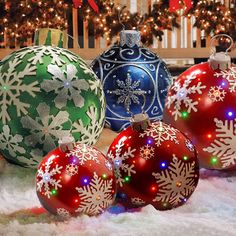 three christmas ornaments sitting on top of snow covered ground next to a tree with lights