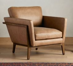 a brown leather chair sitting on top of a wooden floor next to a rug and wall