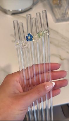 a hand holding five clear tubes with blue and green flowers in them on a marble countertop