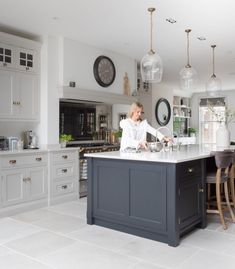 a woman is standing at the center island in a large kitchen with white cabinets and gray countertops