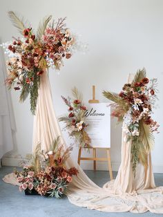 an arrangement of flowers and greenery on display in front of a white board with welcome sign