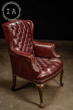 a red leather chair sitting on top of a cement floor next to a black wall