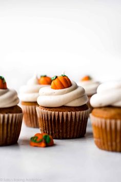 cupcakes with white frosting and pumpkin decorations on top are lined up in rows