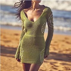 a woman is walking on the beach wearing a green crochet dress with long sleeves