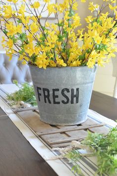 yellow flowers are in a bucket on a dining room table with the word fresh written on it